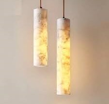 Pair of alabaster cylinder pendant lights suspended from the ceiling with warm internal glow.