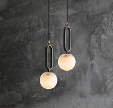 Pair of alabaster globe pendant lights suspended by black metal supports against a textured wall.