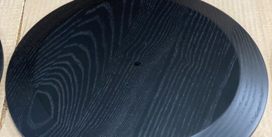 Black-finished ash wood medallion with visible grain and CNC-machined contours.