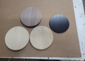 Four round wood lighting bases in walnut, white oak, ash, and black finish with CNC-routed holes.