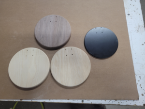 Four round wood lighting bases in walnut, white oak, ash, and black finish with CNC-routed holes.