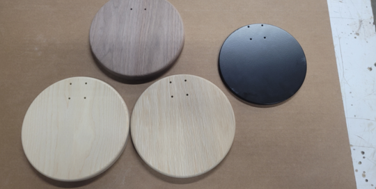 Four round wood lighting bases in walnut, white oak, ash, and black finish with CNC-routed holes.