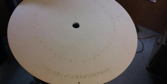 Large MDF base with precision-drilled holes and routed “MODEL of a MASTERPIECE” inscription.