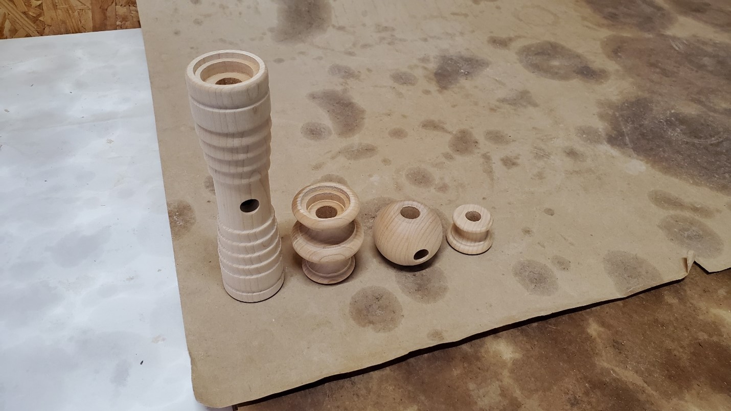 Assorted turned hard maple lighting components with center bores and side holes in various shapes.